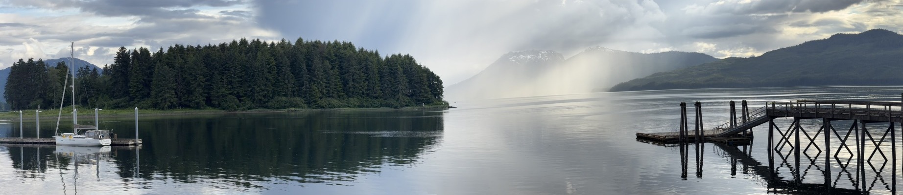 A quiet Pacific Northwest harbor framed by evergreen forest, mountains, and sunbeams